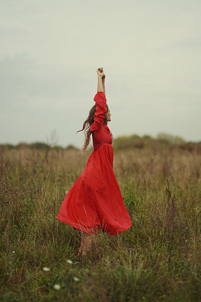 Frau im roten Kleid mit erhobenen Armen auf einer Wiese – Symbol für Freiheit, Selbstbegegnung und erfüllte Partnerschaft.